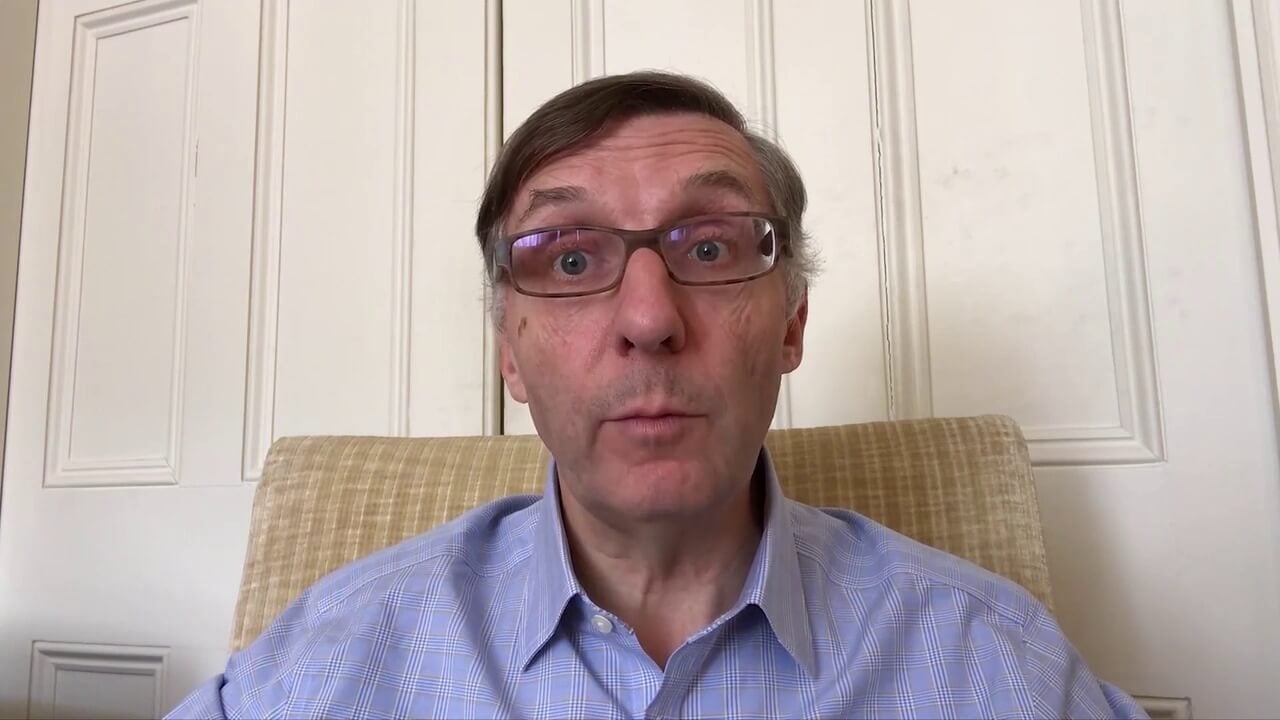 A man with glasses wearing a blue shirt is looking at the camera