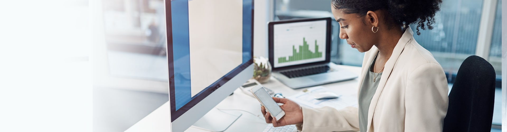 Woman sitting at the desk at work and checking something on the phone