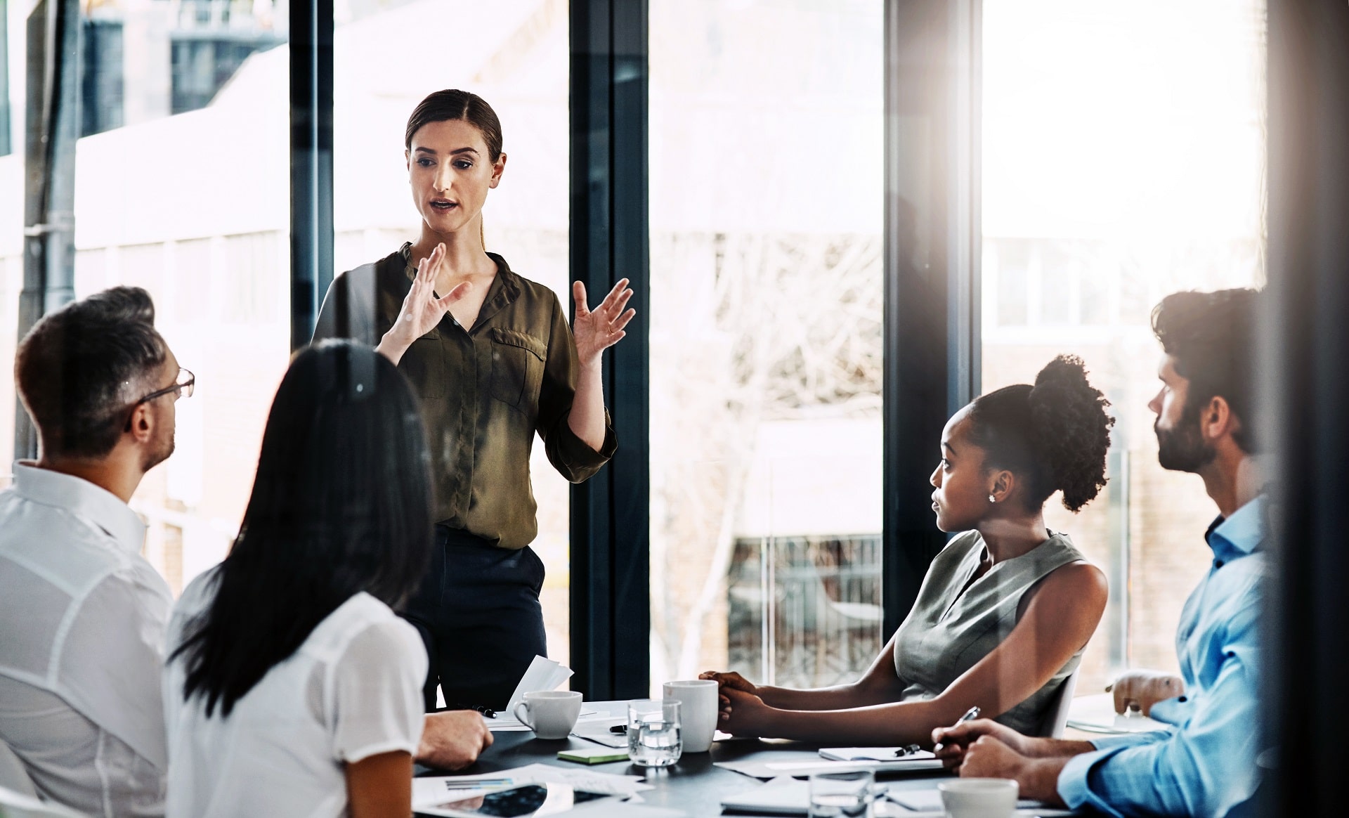 A woman is speaking at a meeting in front of a group of coworkers