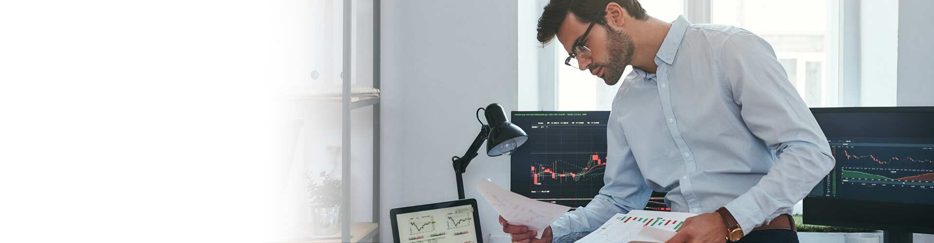 Young businessman sitting at office in front of computer screens with charts