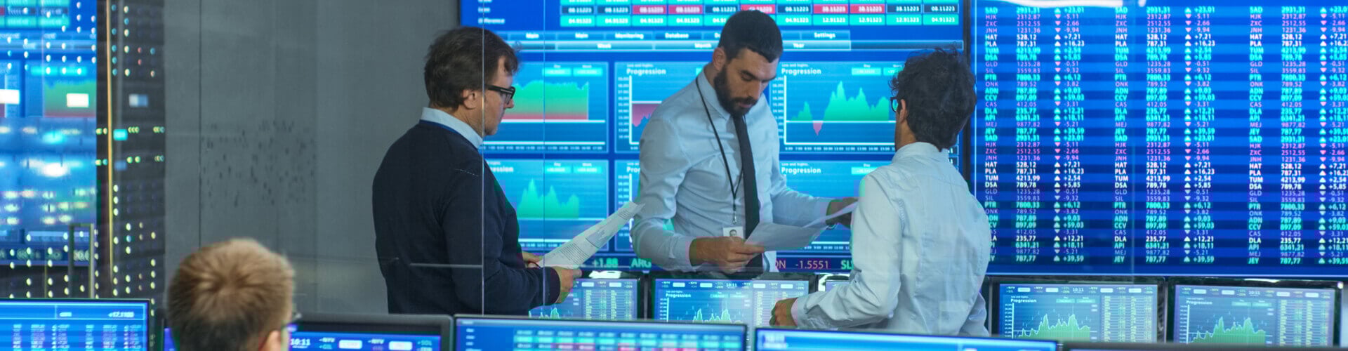 Investment analysts looking at financial data surrounded by computer screens