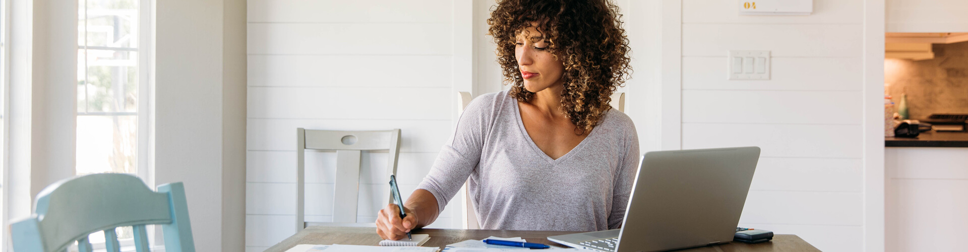A woman sits at the table with an open laptop and takes notes