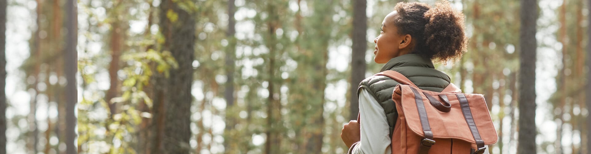 A smiling girl is walking in the woods with an orange backpack