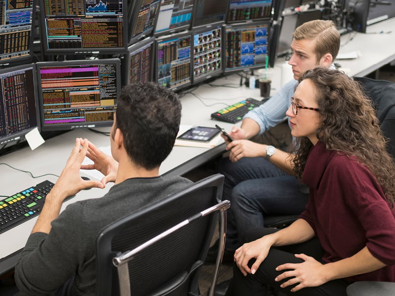 People analyzing data displayed on multiple computer screens