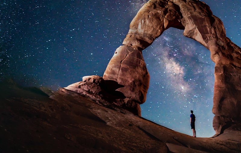 Man under rock arch looking at starry night sky