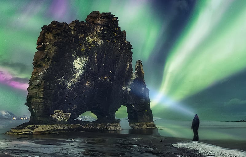 Person looking at rock formation and northern lights