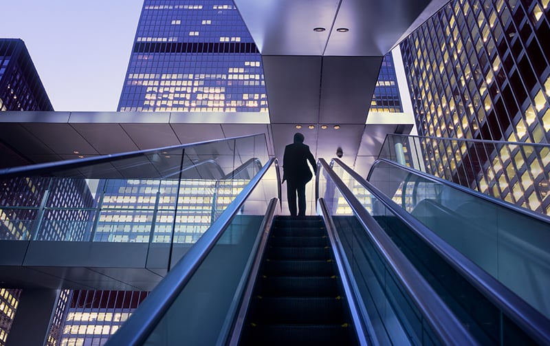 Businessman on top of moving escalator at modern illuminated business district-