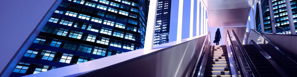 Woman in shadow standing at top of escalator