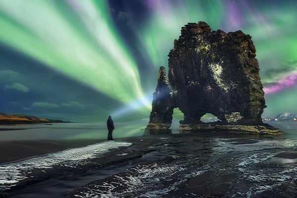 Person looking at rock formation and northern lights