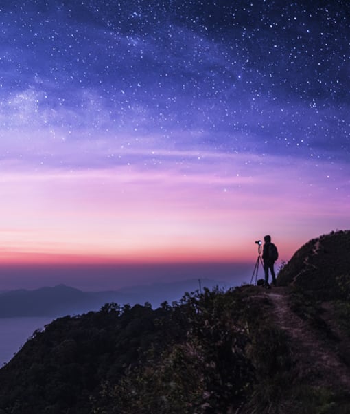 Person standing in the distance with camera overlooking a starry sky