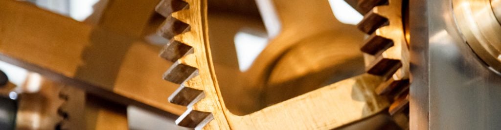 Close-up of interlocking wooden gears with visible teeth, highlighting intricate craftsmanship and texture. Metal components appear on the right side.
