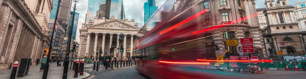 Red London bus driving past London Stock Exchange