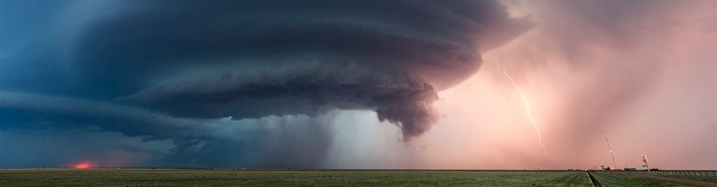 Tornado brewing in a red sunset sky, with road and field in the foreground