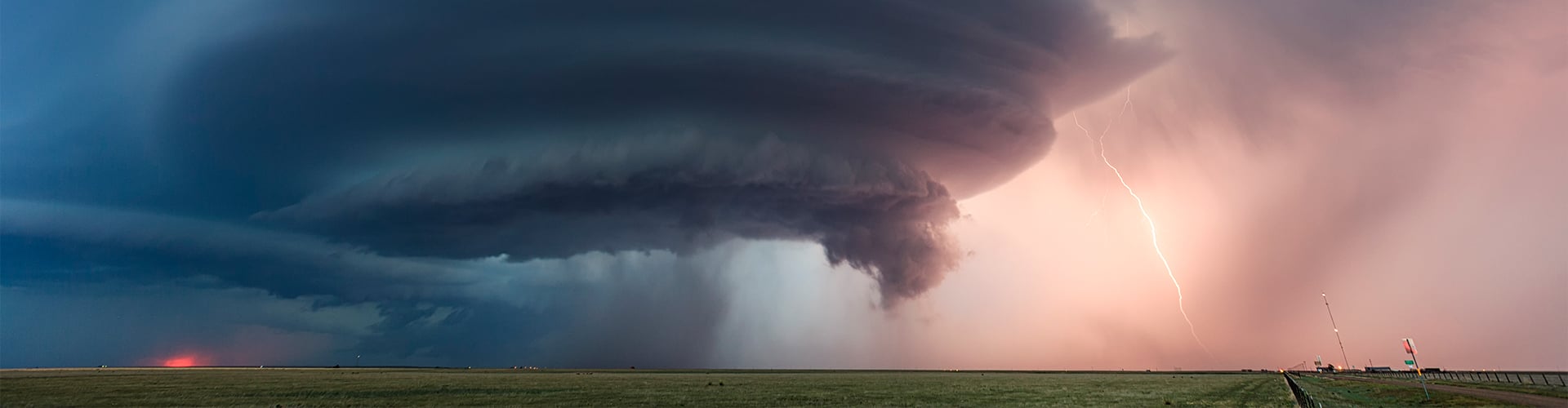 Tornado brewing in a red sunset sky, with road and field in the foreground
