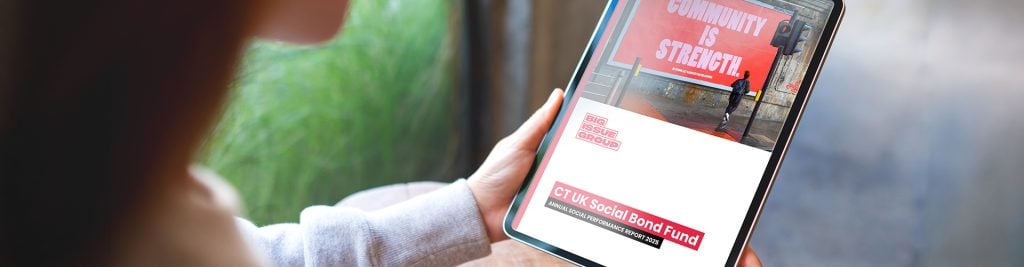 Person holding a tablet displaying CT UK Social Bond Fund content, with a billboard in the background reading “Community is Strength.