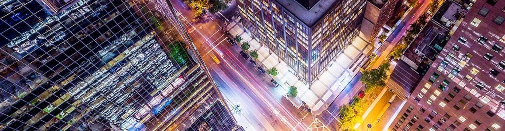 Aerial nighttime view of a modern city intersection surrounded by tall office and residential buildings.