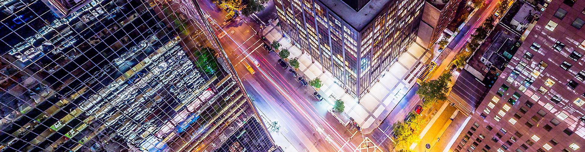 Aerial nighttime view of a modern city intersection surrounded by tall office and residential buildings.