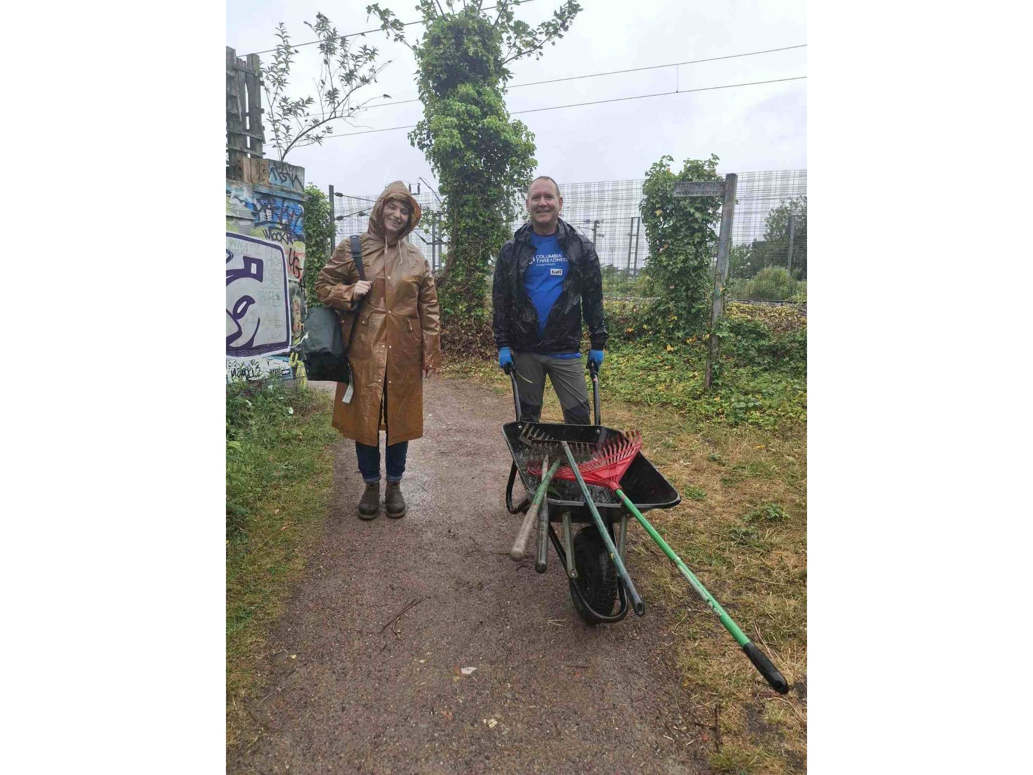 Man and woman from Columbia Threadneedle Investments pushing wheelbarrow in the rain