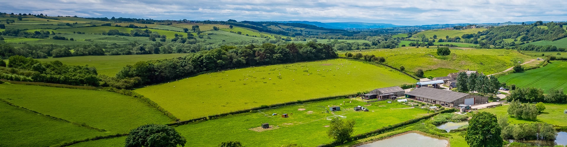 Farm in the middle of rolling green fields, beneath a cloudy but bright sky