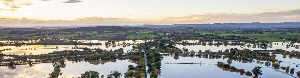 Aerial view of flooded countryside with fields, roads and trees submerged by floodwater at sunset