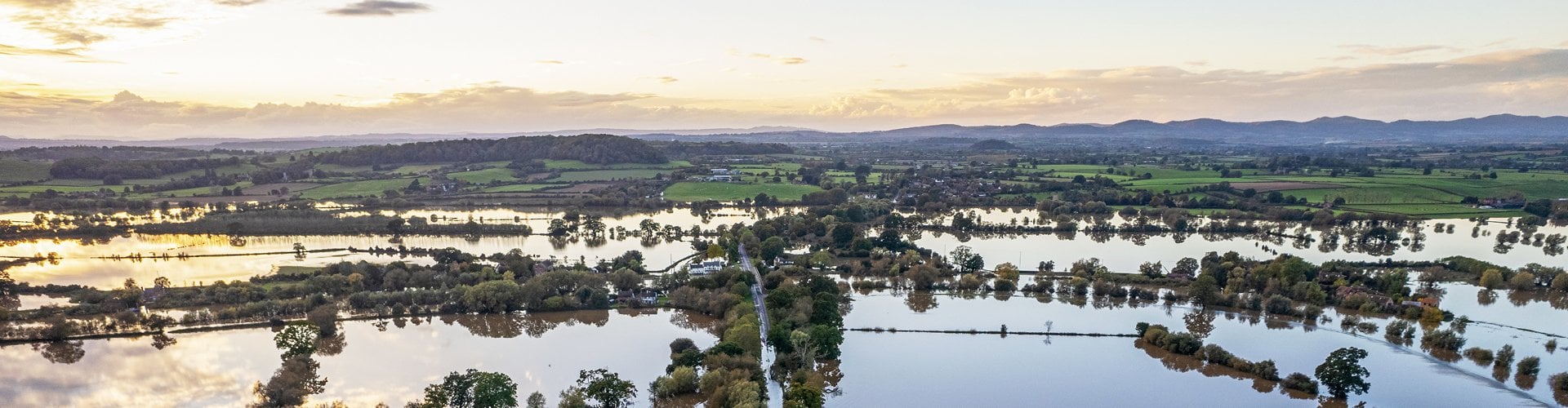 Aerial view of flooded countryside with fields, roads and trees submerged by floodwater at sunset