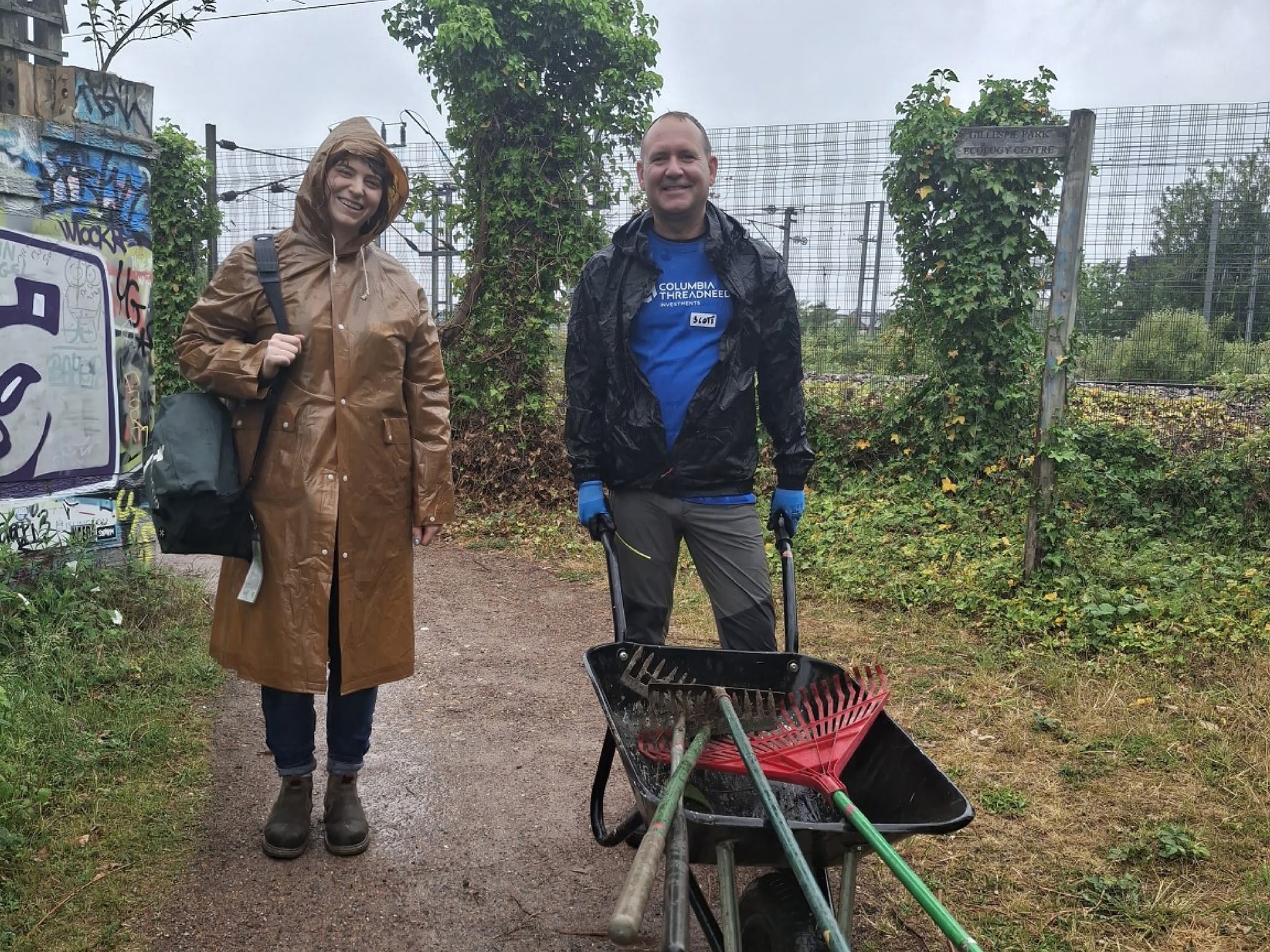 Man and woman from Columbia Threadneedle Investments pushing wheelbarrow in the rain