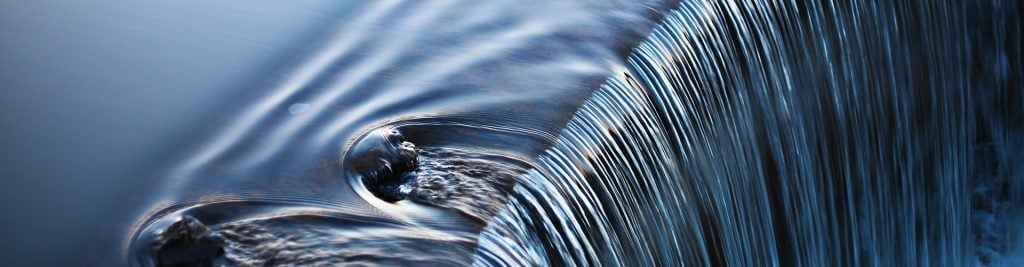 Close-up of flowing water cascading over a small waterfall with ripples and blue reflections.