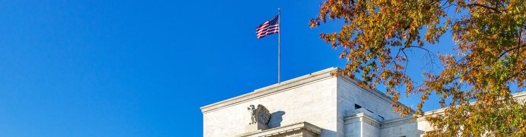 American flag above a white stone building with autumn leaves and blue sky.