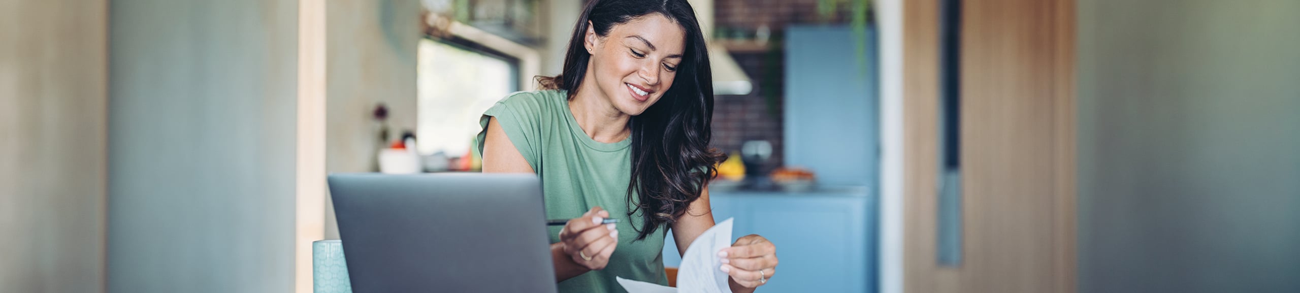 Smiling woman looking at paperwork in front of a laptop