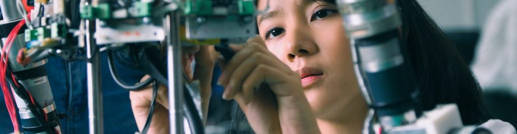 Close-up of a person working on electronic equipment, adjusting wires and components within a complex machine or robotics system in a laboratory or engineering environment.