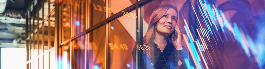 Business professional speaking on a phone in a modern office, overlaid with stock market data and financial chart graphics.
