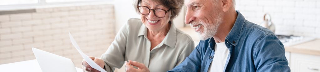 Older couple looking at paperwork and laptop in their kitchen