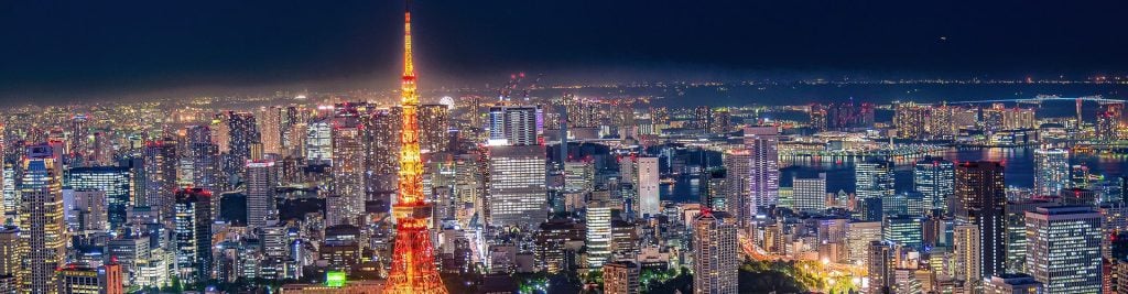 Panoramic nighttime view of Tokyo’s illuminated skyline, with Tokyo Tower prominently lit in orange in the center.
